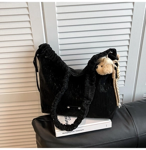Detail of black corduroy tote bag with pleated strap and cute plush bear charm decoration