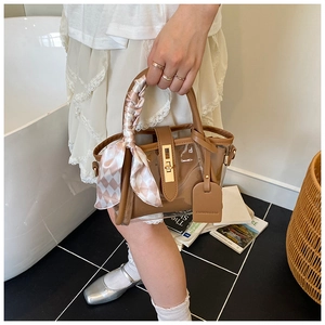 Détail du sac seau en PVC avec bordure en cuir marron, fermoir doré et foulard décoratif