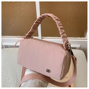 Detail of pink nylon pillow bag featuring pleated handle and metallic logo on textured background