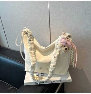 Detail of beige shoulder bag featuring a wide pleated strap and cute teddy bear charm