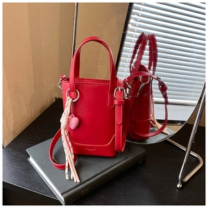 Vue détaillée du mini sac seau rouge avec breloque cœur et pompon sur livres