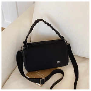 Detail of a black fabric crossbody bag with ruched handle on a white sofa and book