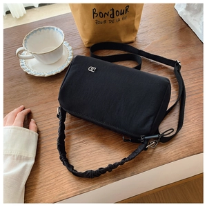 Detail of black nylon crossbody bag with ruched handle on vintage wooden table
