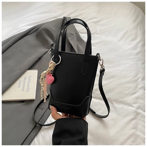Détail d'un mini sac seau noir mat avec un pendentif cœur rose et un ruban rayé élégant