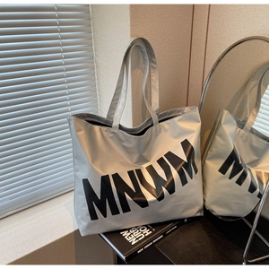 Close-up of metallic silver tote bag with black MNWM letter print on industrial surface