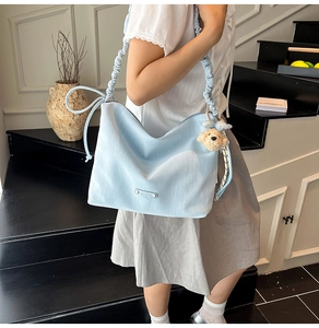 Detailed view of light blue textured shoulder bag with plush bear charm on a staircase