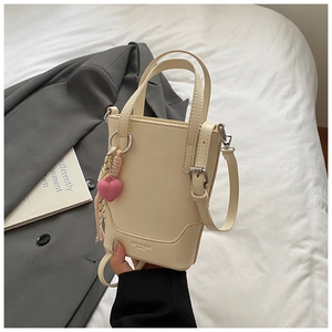 Détail d'un mini sac seau beige avec pendentif coeur rose et ruban sur tissu de costume