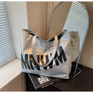 Detail of silver metallic tote bag with black MNVM letters and wide shoulder straps