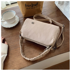 Close-up of beige nylon crossbody bag with adjustable wide strap and pleated handle detail