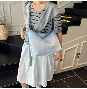 Detail of light blue shoulder bag featuring a unique pleated strap and metal logo plaque