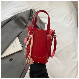 Gros plan sur le sac seau en cuir rouge avec breloque cœur rose et détail de corde