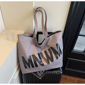 Detail of the large mauve tote bag with black MNWM letters leaning against a suitcase