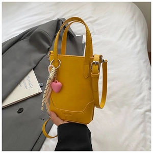 Détail d'un sac seau jaune avec breloque cœur rose sur lin blanc et veste grise