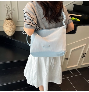 Detail of light blue shoulder bag with pleated scrunchie strap and silver metal plaque