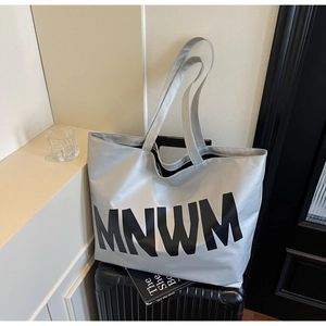 Detail of large silver-grey tote bag with MNWM letters placed on a travel suitcase