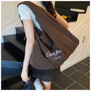 Detail view of large brown plaid tote bag with Our Fan Party script print and wide strap