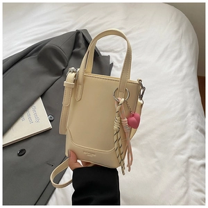Gros plan d'un sac seau crème avec breloque cœur rose sur fond de lit élégant