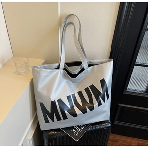 Silver large tote bag with MNWM letters placed on a suitcase for travel and commute