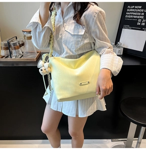 Detail of light yellow shoulder bag with ruched strap and white plush toy pendant