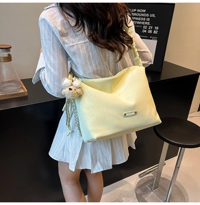 Detail of light yellow shoulder bag with ruched strap and cute white bear pendant charm