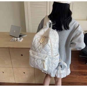 Detailed close-up of white quilted backpack featuring pearly sheen and braided zipper detail