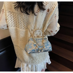 Dettaglio della pochette in broccato blu con ricami floreali dorati e catena di perle
