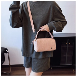 Detail of pink crossbody bag with pleated handle and metallic logo on casual outfit