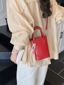 Sac seau en cuir rouge avec breloque cœur porté par un mannequin sur des escaliers