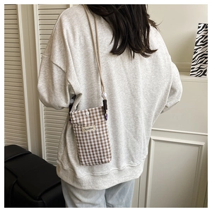 Detail of checkered canvas mini phone bag with Sozakka tag worn with casual street outfit