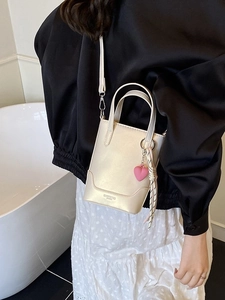Sac seau chic crème avec pendentif cœur, porté en bandoulière sur l'épaule d'un mannequin