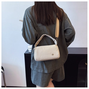 Detail view of stylish cream crossbody pillow bag with ruched handle and metal logo