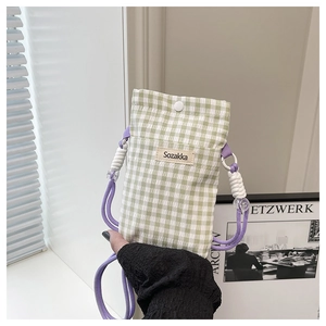 Close-up of green gingham fabric crossbody bag with purple cord strap and logo label