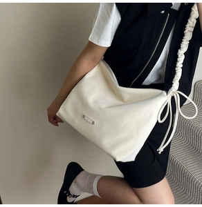 Detail of creamy white leather tote bag with pleated shoulder strap and metal hardware