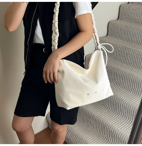 Detail of cream-white shoulder bag featuring a stylish ruched strap and silver metal logo
