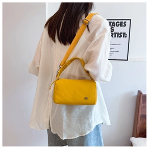 Close-up of bright yellow crossbody bag with pleated handle and metal logo detail