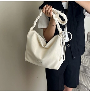 Close-up of cream hobo bag with ruched strap and side drawstring detail on a model