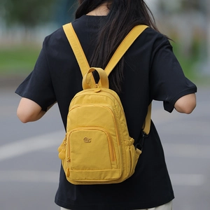 Rear view of a model wearing a bright yellow waterproof nylon multi-pocket mini backpack