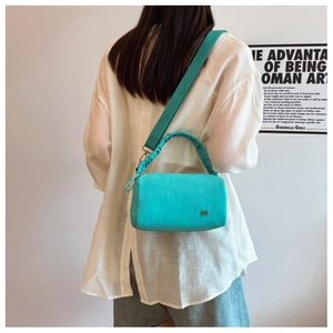 Detailed view of women's cyan crossbody pillow bag worn by model in a minimalist setting