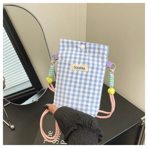 Detail of blue gingham fabric crossbody bag with colorful woven strap and brand label