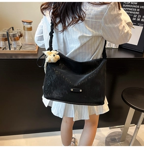 Detail view of black textured tote bag with pleated strap and beige teddy bear charm