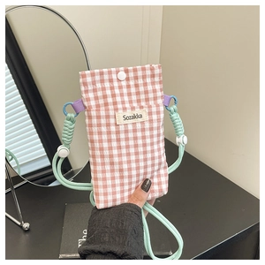 Detail view of red checkered canvas bag with green rope strap and white button closure