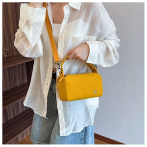 Detail of yellow canvas crossbody bag with silver logo and ruffled handle on white shirt