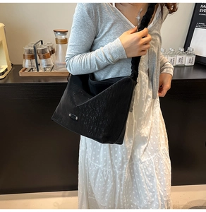 Detail of black tote bag with brushed texture and ruched shoulder strap in a cozy cafe setting