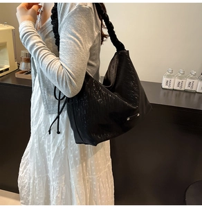 Detail view of black textured tote bag with ruched shoulder strap on model