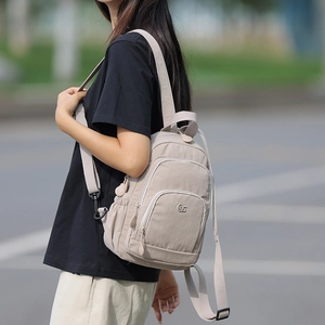 Detail of light apricot nylon backpack showing multiple zipper pockets and brand logo