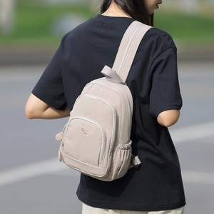 Detail of beige nylon crossbody bag showing multiple zip pockets and brand logo logo on back