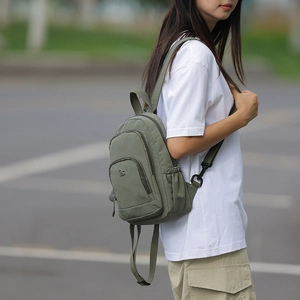 Detail view of army green nylon backpack with multiple pockets worn by a model in nature