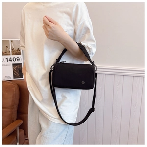 Detail of black nylon crossbody bag featuring pleated handle and metallic logo plaque