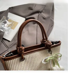 Detail of straw woven tote bag featuring leather handles and pearl bow charm accessory