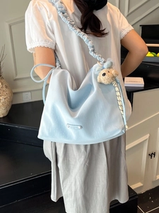 Light blue slouchy tote bag with ruffled shoulder strap and teddy bear charm accessory